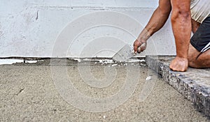 Installing new pavement or floor outside from large concrete tiles, closeup detail on male worker fixing sand and gravel