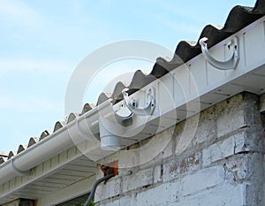 Installing plastic roof gutter holder for dowspout drain pipe outdoor. Plastic roof guttering, rain guttering