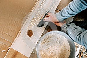 Installing wooden hardwood floor, detail on man hands holding wooden tile and spreading glue on parquet