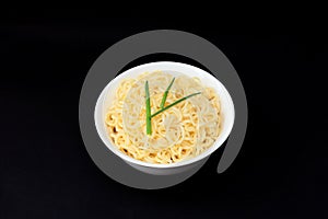 Instant Chinese curly noodles in white bowl on black background. Selective focus. Asian food concept. Unhealthy eating