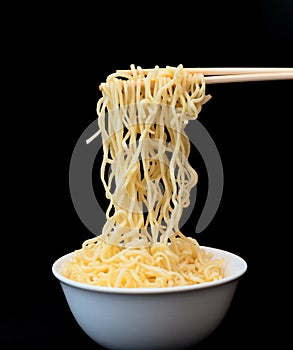 Instant Chinese curly noodles in white bowl with wood sticks on black background. Selective focus. Asian food concept