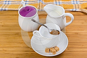 Instant coffee granules in spoon atop empty cup, milk, sugar