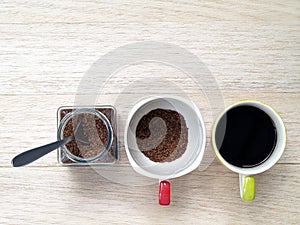 instant coffee powder with silver spoon in glass jar and cup and black coffee in another one cup on wooden desk floor
