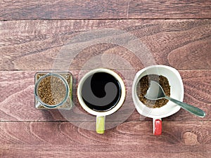 instant coffee powder in transparent glass jar and one cup of black coffee and prepare to brew another cup with silver teaspoon