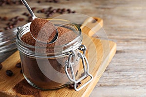 Instant coffee and spoon above glass jar on wooden table, closeup. Space for text