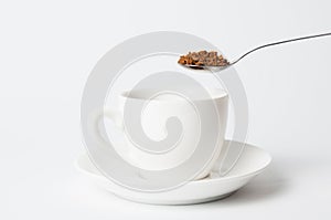 Instant coffee spoon over white cup on white background