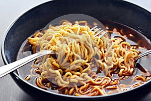 Instant noodle soup with fork and spoon in a bowl. Spicy noodles.