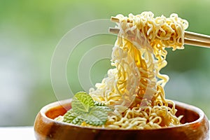 Instant noodle in wooden bowl with bamboo chopstick on green background