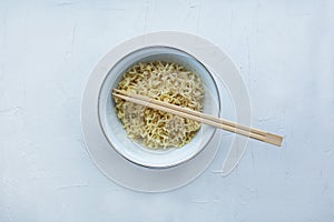 Instant noodles in a bowl with wooden chopsticks on a white textured background