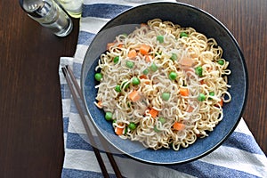 Instant noodles with carrots and peas in a blue bowl.