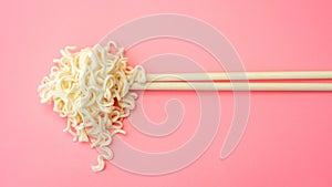 Instant noodles and chopsticks on a pink background