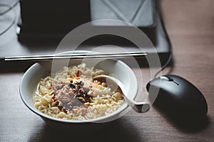Instant noodles with seasoning garnish and Hot water in bowl on working space with laptop and mouse in house- work from home