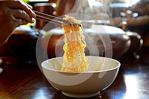 Instant noodles soup with chopsticks in hand on wooden table background with smoke. Foods concept. Dark tone