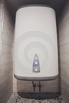 Instant tankless electric water heater installed on white tile wall with input and output pipe outlet and elcb safety