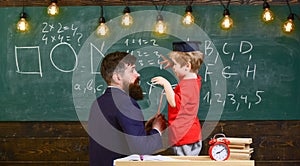 Instructive conversation concept. Child in graduate cap listening teacher, chalkboard on background, rear view. Teacher