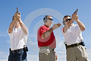 Instructor Assisting Men With Hand Guns At Firing Range