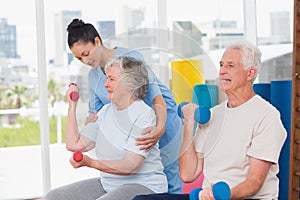 Instructor assisting senior woman in lifting dumbbells by man