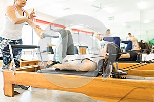 Instructor Assisting Woman On Reformer Machine In Gym