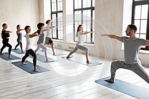 Instructor with diverse people practicing yoga, doing Warrior two exercise