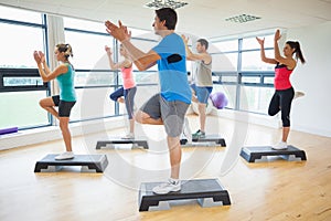 Instructor with fitness class performing step aerobics exercise