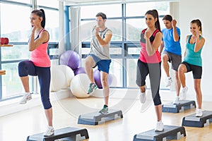 Instructor with fitness class performing step aerobics exercise