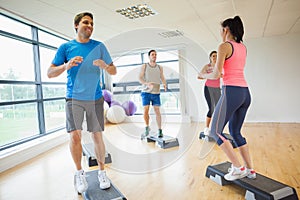 Instructor with fitness class performing step aerobics exercise