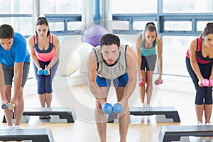 Instructor with fitness class performing step aerobics exercise with dumbbells