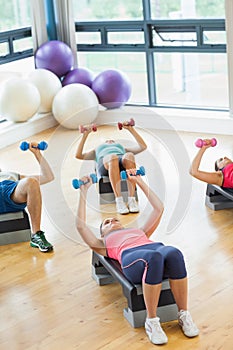 Instructor with fitness class performing step aerobics exercise with dumbbells