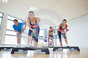 Instructor with fitness class performing step aerobics exercise with dumbbells