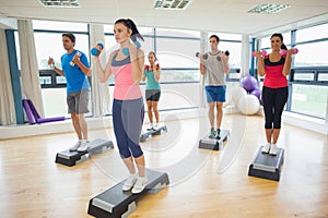 Instructor with fitness class performing step aerobics exercise with dumbbells