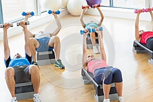 Instructor with fitness class performing step aerobics exercise with dumbbells