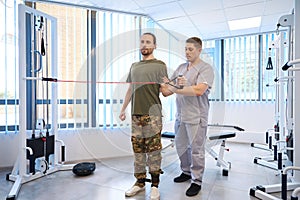 Instructor helps weakened patient in physiotherapy room of rehabilitation center