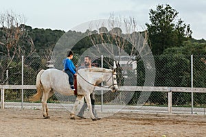 Instructor leading a horse with a child in an equine therapy session. People with disabilities