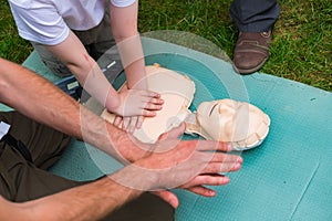 Instructor show how to give the first aid heart compressions using dummy during the children training outdoors