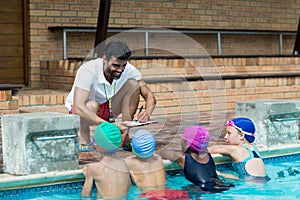Instructor writing on clipboard while explaining little swimmers at poolside