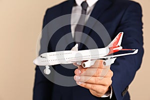 Insurance agent holding toy plane on color background, closeup.