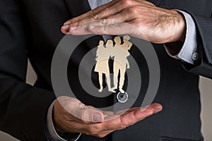 Insurance agent making protecting gesture around a paper cut silhouette of a family