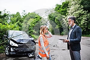 An insurance agent talking to a woman driver by the car on the road after an accident.