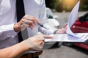 Insurance agent writing on clipboard while examining car after accident claim being assessed and processed