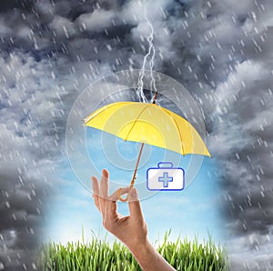 Insurance concept. Man covering medical kit illustration with yellow umbrella during storm, closeup