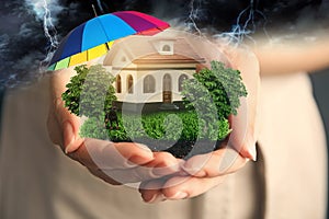 Insurance concept - umbrella demonstrating protection. Woman holding house model with green lawn