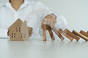 insurance with hands protect a house. The wooden domino block is about to fall on the house. Home insurance or house insurance con