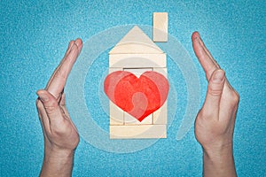 Insurance home concept. House from wooden bricks inside hands. House with red heart. Love in home concept. Protection home