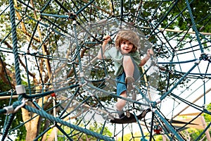 Insurance kids. Happy little child boy sitting on the web on playground and ready to jump. Happy kids, healthy teenager