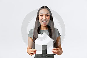 Insurance, loan, real estate and family concept. Cheerful asian female buying or selling home, holding paper house and