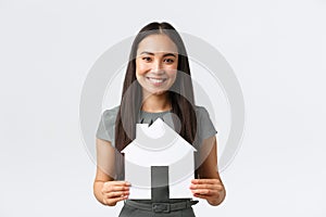 Insurance, loan, real estate and family concept. Smiling asian woman buying home, holding paper house in hands and