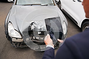 Insurance Loss Adjuster Taking Picture With Digital Tablet Of Damage To Car From Motor Accident