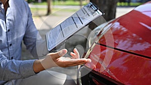 Insurance officer examining car and filing report claim form after accident.