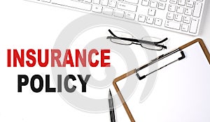 INSURANCE POLICY text written on the white background with keyboard, paper sheet and pen