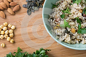 Integral rice in green bowl, cooked with almond, pumpkin seeds, chick-pea and sprinkled with parsley on wooden background.